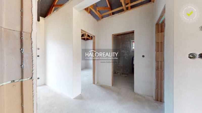 Interiér rodinného domu s neomítnutými stěnami a viditelnou střešní konstrukcí.