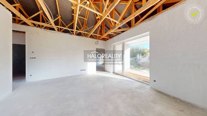 Interiér rodinného domu s odkrytým stropem a velkými prosklenými dveřmi.