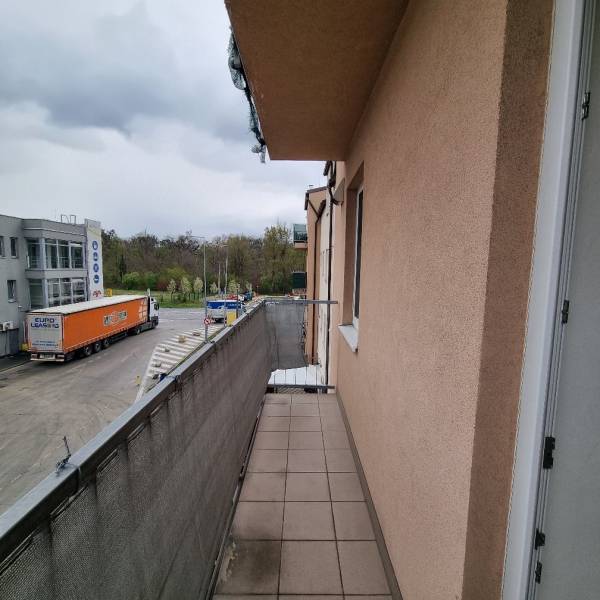 Balkon garsonky na Pezinské ulici v Malackách s výhledem na parkoviště a zeleň.