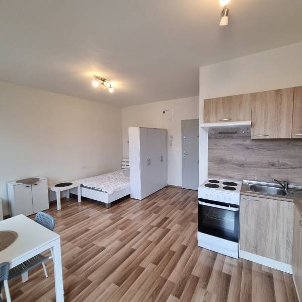 Garsonka s kuchyňským koutem, křeslem a podlahou s dřevěným dekorem.