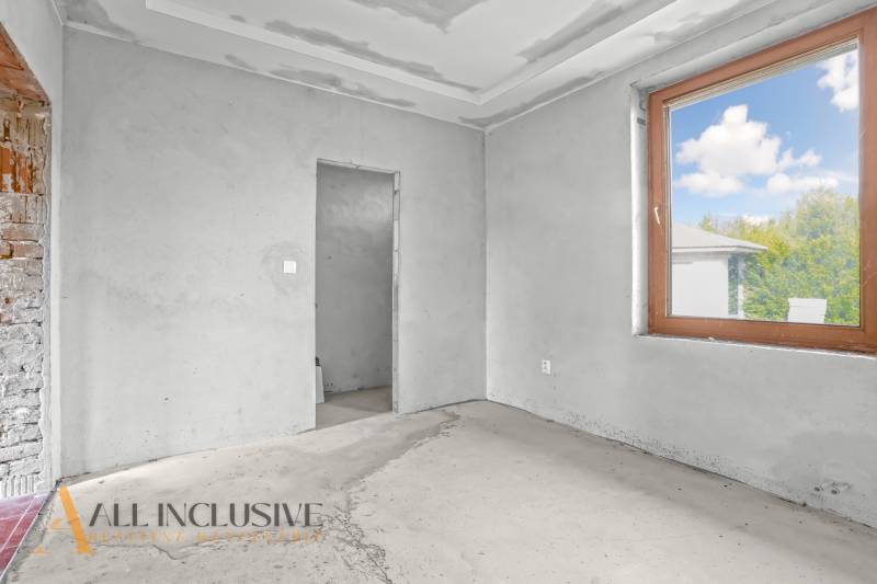 Interiér rodinného domu s nedokončenými stěnami a velkým oknem.