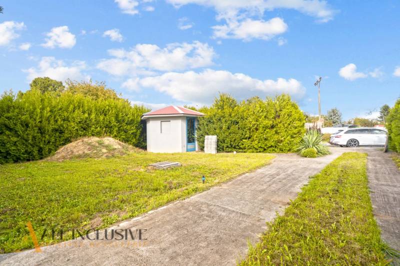 Dvůr u rodinného domu v Bátorových Kosihách s trávníkem a zahradním domkem.