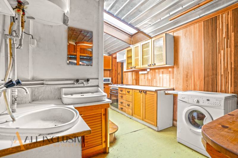 Kuchyně v rodinném domě s dřevěnými skříňkami, dřezem a pračkou.