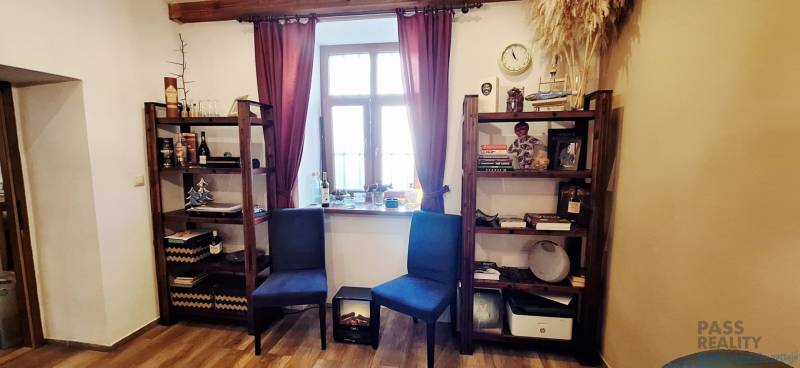 Knihovny s dekoracemi, židle a okno s bordovými závěsy v obchodním prostoru.