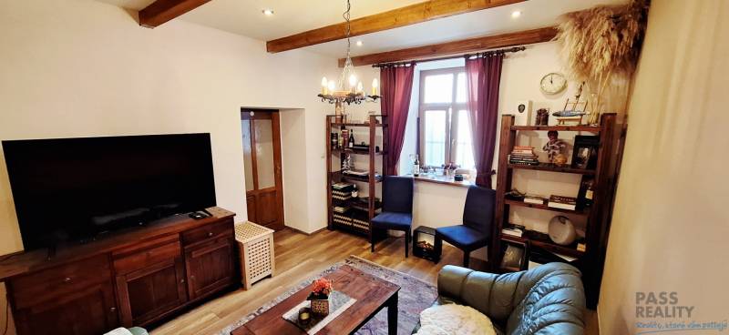 Obývací pokoj s podlahou s dřevěným dekorem, televizorem, policemi a pohodlným nábytkem.