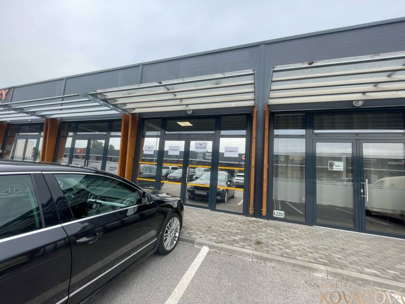 Obchodní prostory na Brněnské ulici v Trenčíně se skleněnou fasádou a parkovištěm.