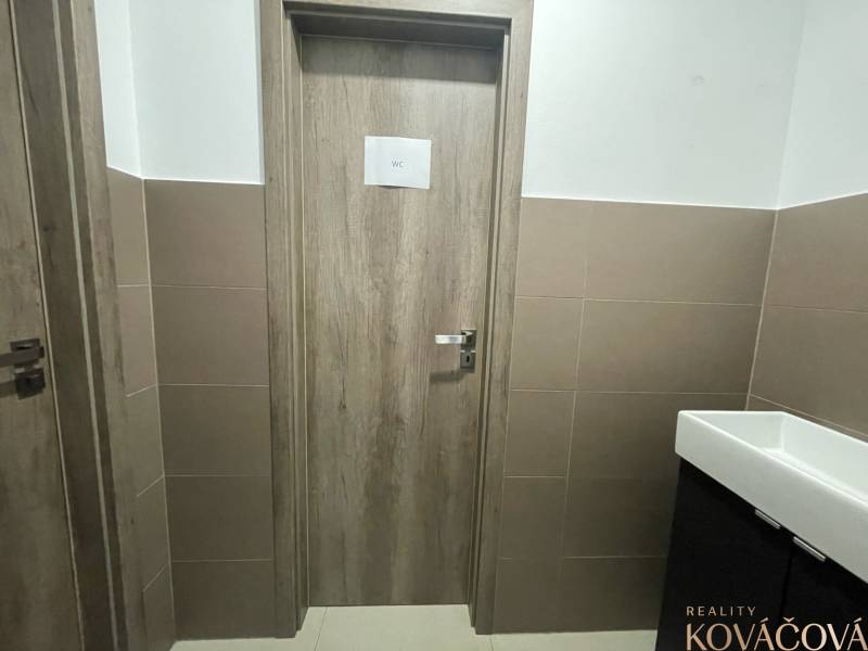 Interiér obchodních prostor s dveřmi na WC, obložené stěny, keramické umyvadlo.