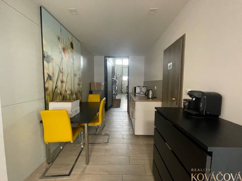 Obchodní prostory s jídelním stolem, žlutými židlemi a kuchyňkou.