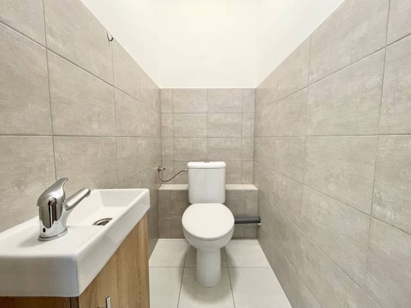 Toaleta s šedými obklady a umyvadlem v kanceláři.