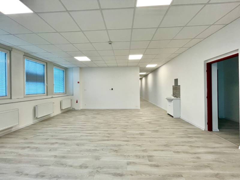 Kanceláře s podlahou s dřevěným dekorem, bílými stěnami a velkými okny.