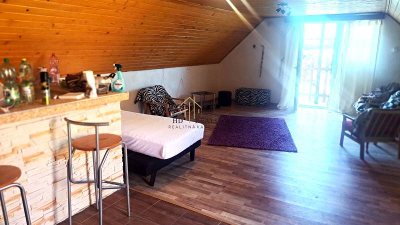 Interiér chaty s barovým pultem, postelí a podlahou s dřevěným dekorem.