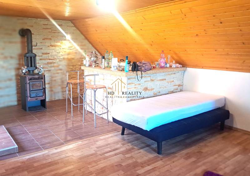 Interiér chaty s krbem, barovým pultem a podlahou s dřevěným dekorem.