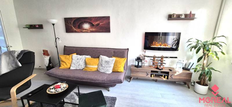 Obývací pokoj v 2-pokojovém bytě s pohovkou, policí a elektrickým krbem.