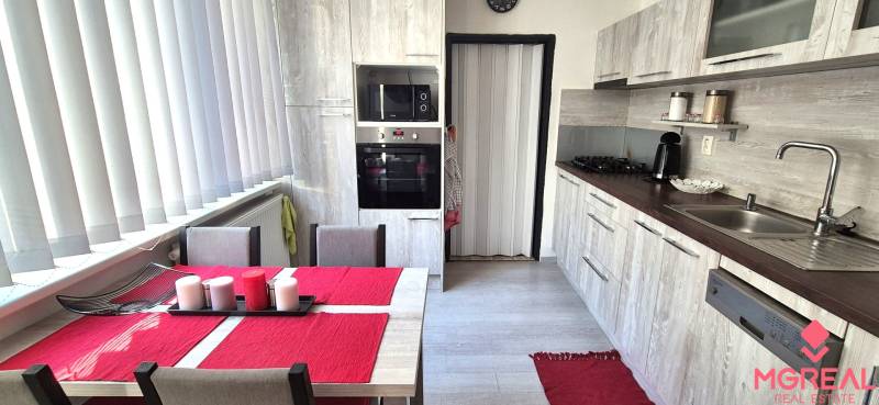 Kuchyně s jídelním stolem, bílými žaluziemi a kuchyňskou linkou v 2-pokojovém bytě.