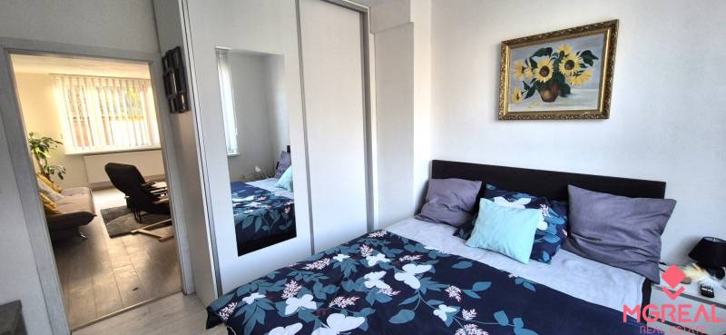 Ložnice s barevnou postelí a skříní v dvoupokojovém bytě, vede do obývacího pokoje.