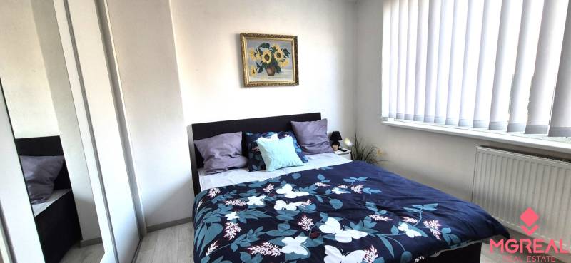 Ložnice v 2pokojovém bytě s postelí, obrazem a zrcadlovou skříní.