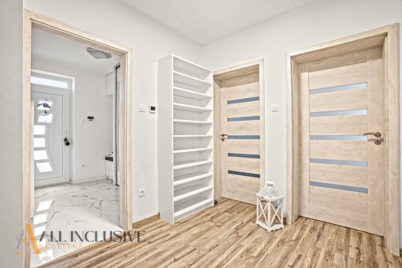 Interiér rodinného domu s podlahou s dřevěným dekorem, dveřmi a bílým regálem.