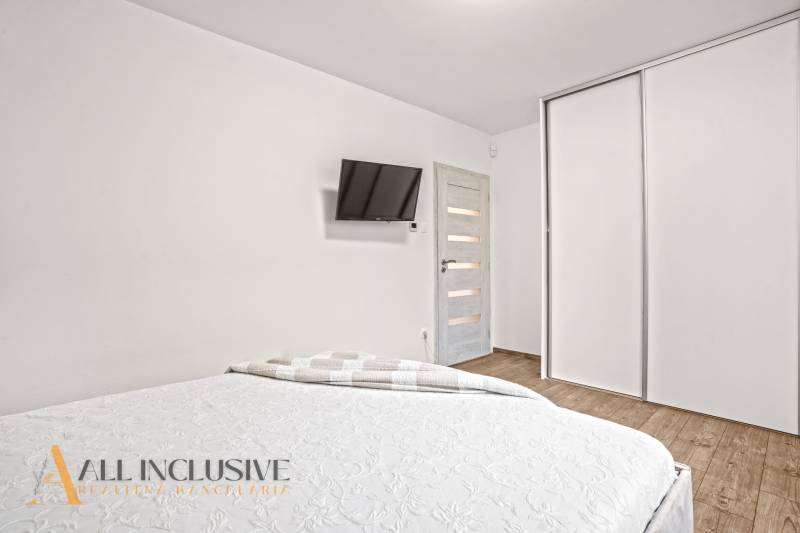 Ložnice v rodinném domě s bílými skříněmi, TV na stěně a podlahou s dřevěným dekorem.