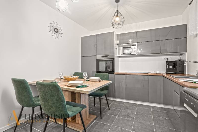 Kuchyně v rodinném domě s šedou linkou, jídelním stolem a zelenými židlemi.