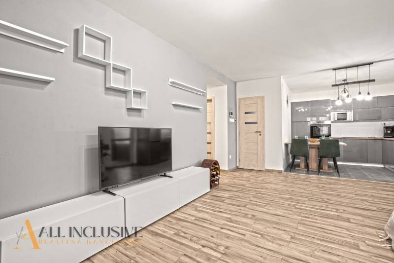 Obývací pokoj v rodinném domě s podlahou s dřevěným dekorem, televizorem, jídelním stolem a kuchyní.