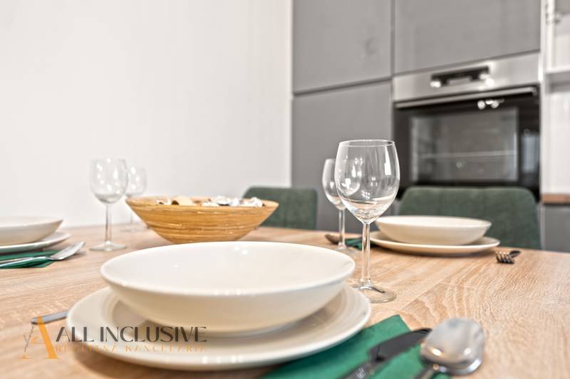 Jídelní stůl s prostíráním a sklenicemi, v pozadí kuchyně v rodinném domě.