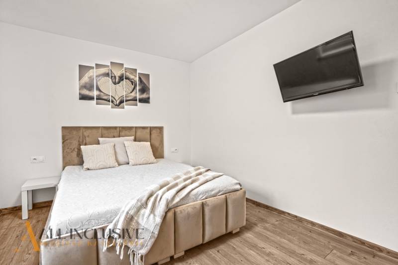 Ložnice v rodinném domě s pohodlnou postelí, televizí a podlahou s dřevěným dekorem.