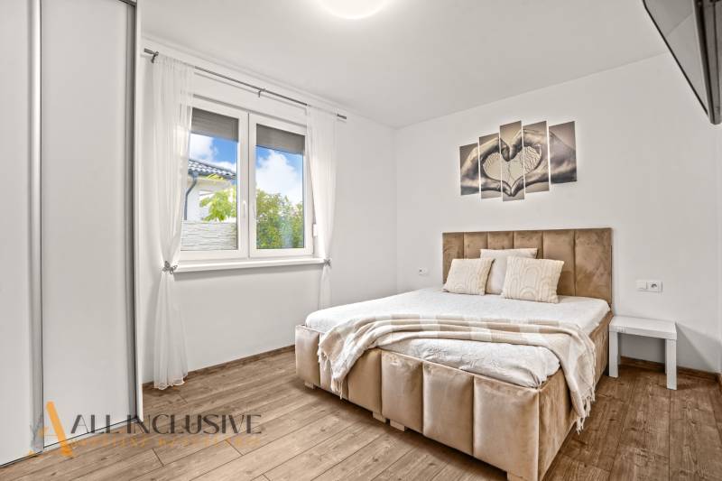 Ložnice se světlým rámem postele, podlahou s dřevěným dekorem a nástěnným obrazem v rodinném domě.