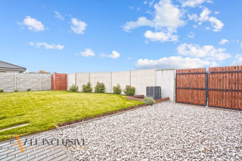 Zahrada u rodinného domu v Gabčíkově s trávníkem, kamínky a dřevěným plotem.