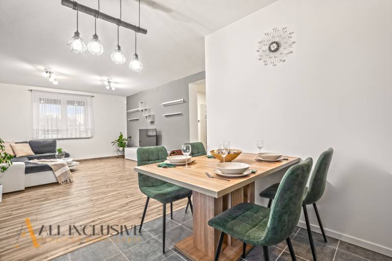 Interiér rodinného domu s podlahou s dřevěným dekorem, jídelní stůl a zelené židle.