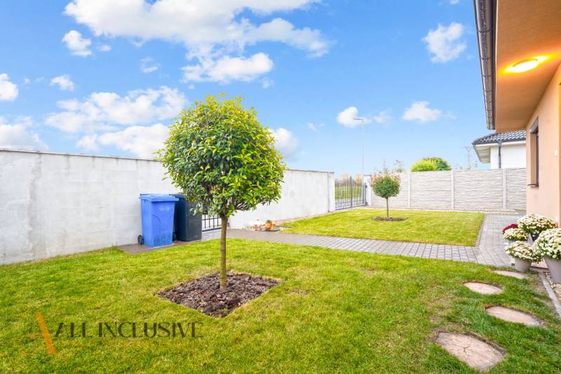 Zahrada rodinného domu v Gabčíkově s trávníkem, stromem a chodníkem vedle plotu.