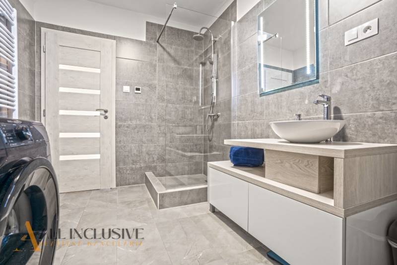 Koupelna se sprchou, umyvadlem na dřevěné desce a pračkou v rodinném domě.