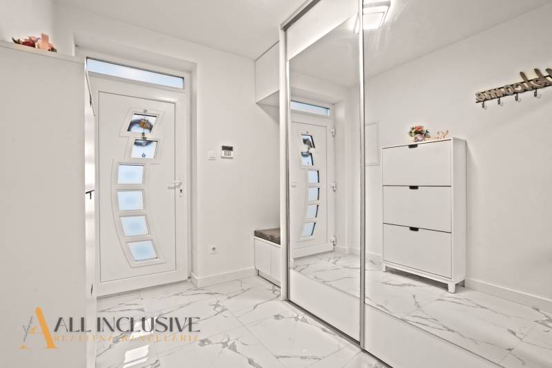 Interiér rodinného domu s bílými skříněmi, zrcadlem a podlahou s mramorovým dekorem.