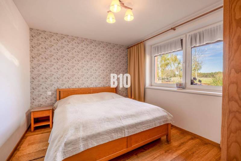 Ložnice v rodinném domě s květovanou tapetou a podlahou s dřevěným dekorem.