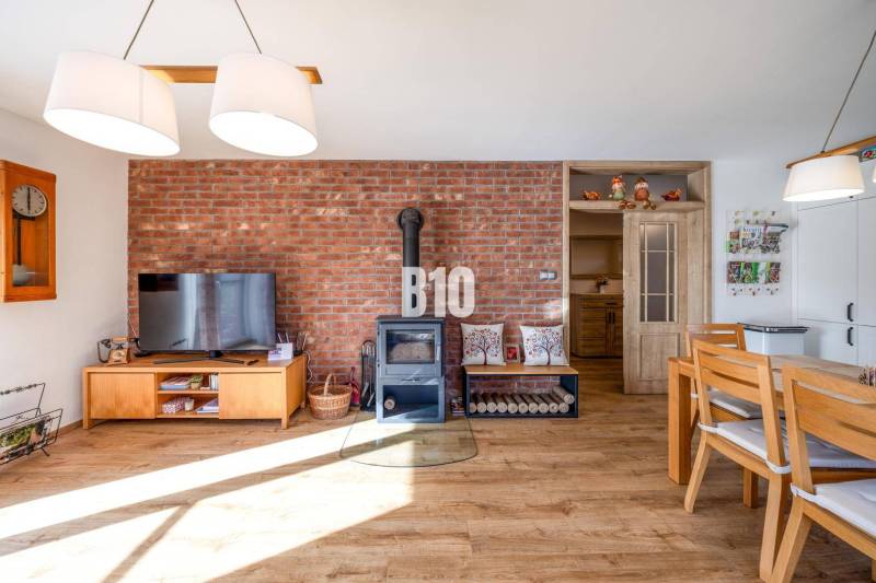 Interiér rodinného domu s cihlovou stěnou, kamny a podlahou s dřevěným dekorem.