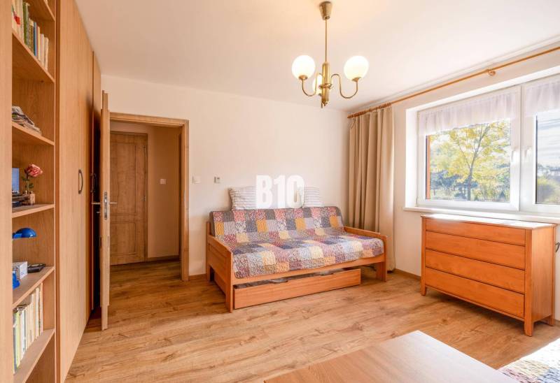 Pokoj v rodinném domě s podlahou s dřevěným dekorem, sedačkou a komodou.