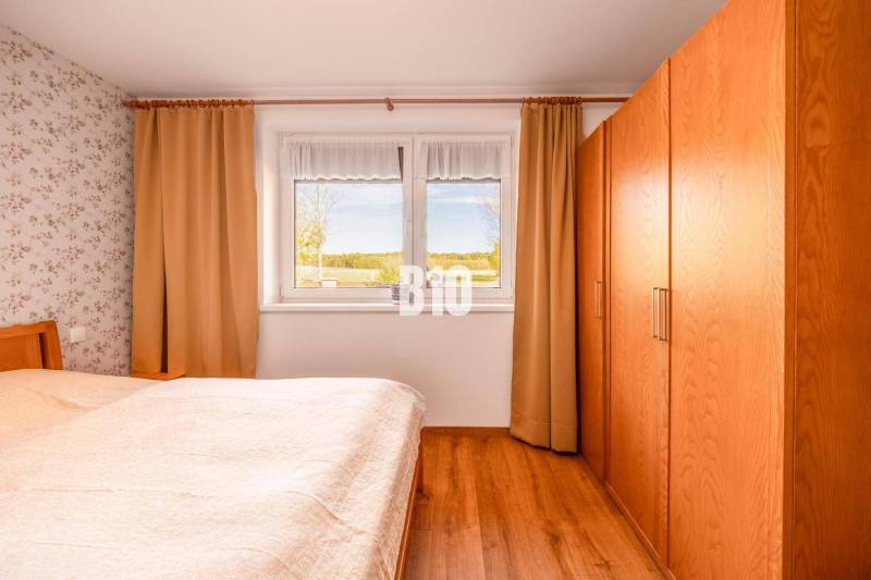 Ložnice v rodinném domě s podlahou s dřevěným dekorem a výhledem z okna.