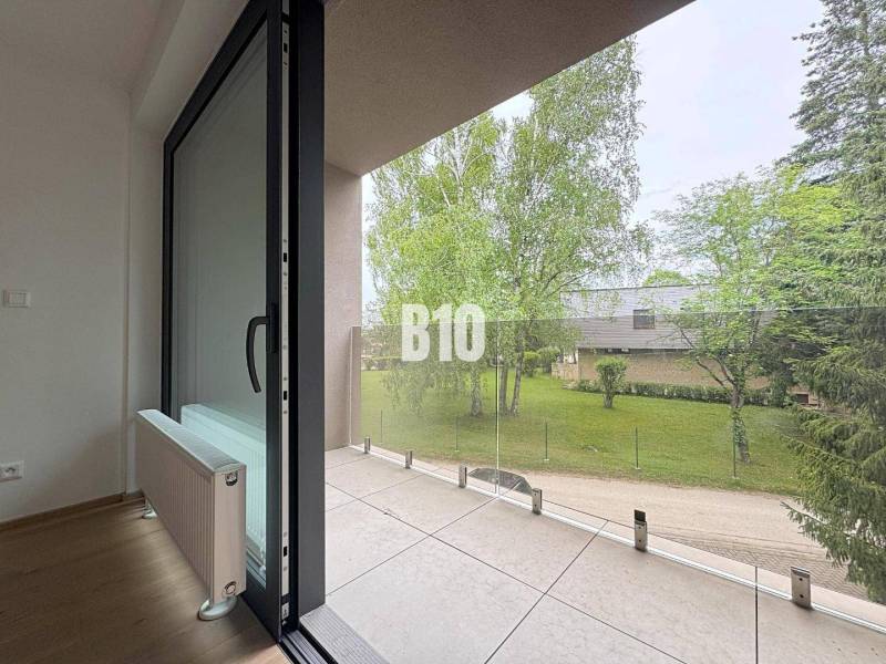 Balkon 2pokojového bytu s výhledem na zeleň a proskleným zábradlím.