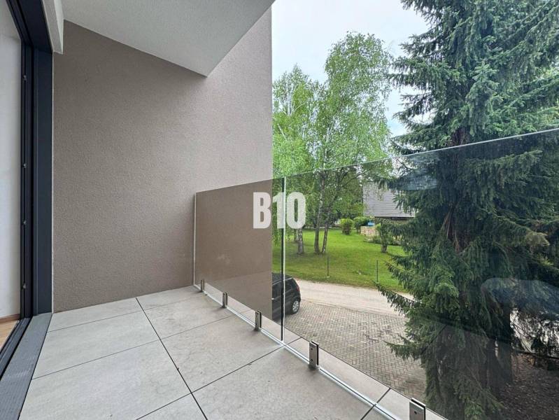 Balkon se skleněným zábradlím nabízející výhled na zeleň v 2pokojovém bytě.