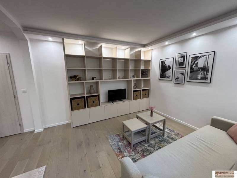 Obývací pokoj v 2-pokojovém bytě s pohovkou, policí a podlahou s dřevěným dekorem.