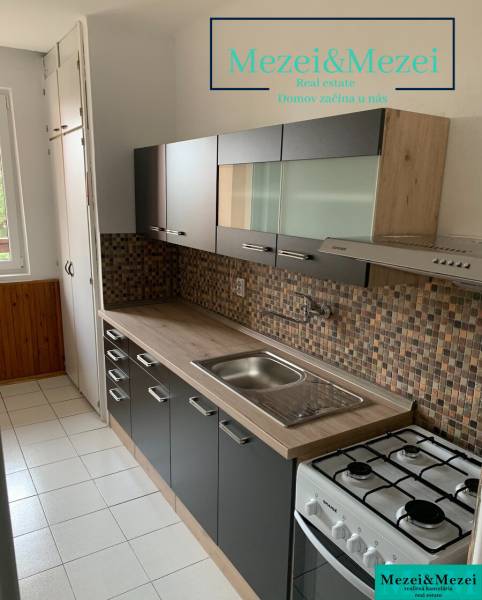 Kuchyně v 2-pokojovém bytě s tmavým nábytkem a kachličkovým obkladem.