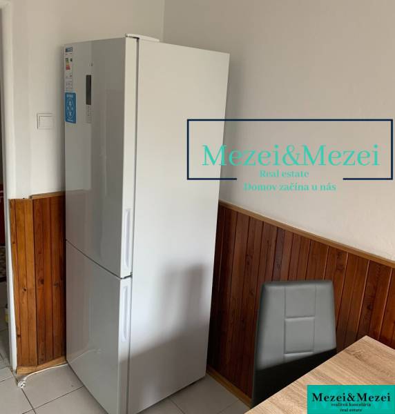 Kuchyně v 2pokojovém bytě, lednice, dřevěný obklad, šedá židle, jídelní stůl.