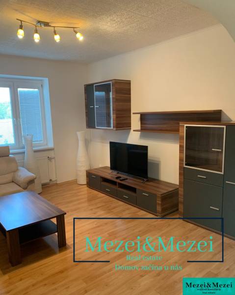 Obývací pokoj s dřevěným dekorem podlahy, televizorem a pohodlnou sedačkou v 2-pokojovém bytě.