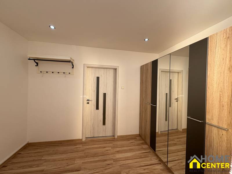 Pokoj v 3-pokojovém bytě s podlahou s dřevěným dekorem a zrcadlovou skříní.