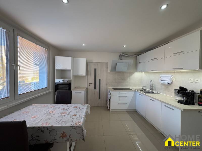 Kuchyně ve 3-pokojovém bytě s bílými skříňkami a obkladem, podlaha s dřevěným dekorem.