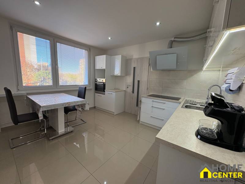 Kuchyně 3pokojového bytu s velkými okny, jídelním stolem a světlou podlahou.