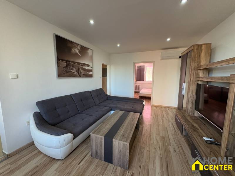 Obývací pokoj v 3-pokojovém bytě s rohovou sedačkou a podlahou s dřevěným dekorem.