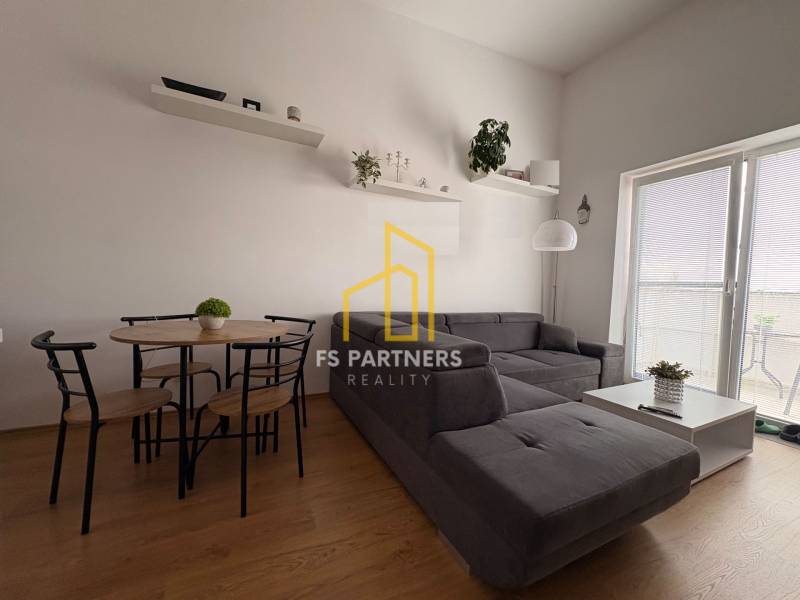 Obývací pokoj s tmavě šedou pohovkou a podlahou s dřevěným dekorem v 2-pokojovém bytě.