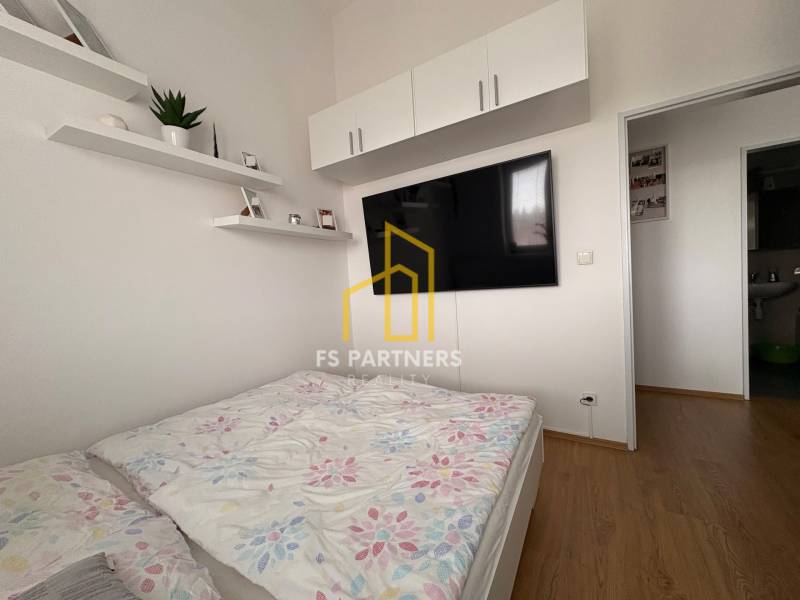 Světlá ložnice v 2-pokojovém bytě s TV a podlahou s dřevěným dekorem.