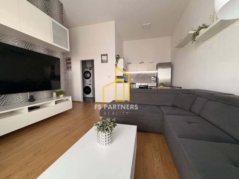 Obývací pokoj s velkou sedačkou, podlahou s dřevěným dekorem a televizorem v 2-pokojovém bytě.