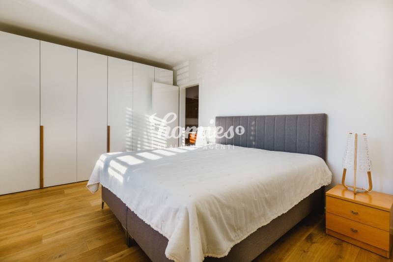 Ložnice s velkou postelí, šatní skříní a podlahou s dřevěným dekorem v rodinném domě.